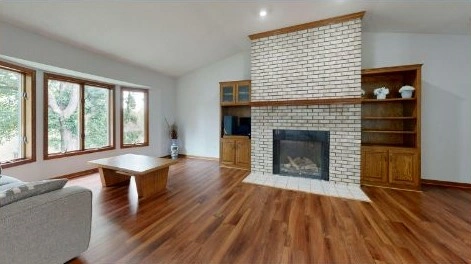 Traditional living room with white brick fireplace, wooden shelves, and large windows.
