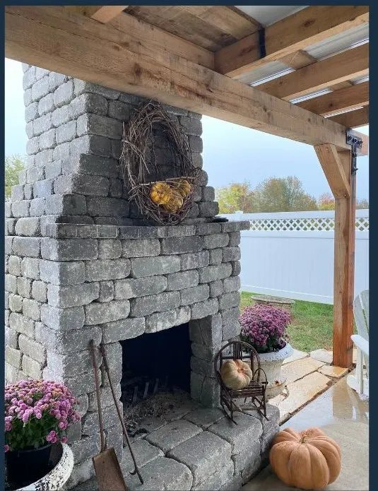 Outdoor stone fireplace with a rustic design, decorated with pumpkins and potted plants