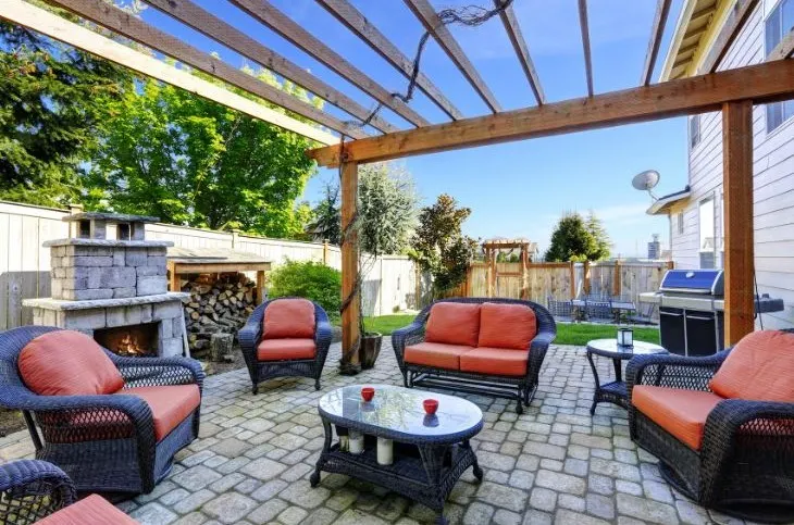 Outdoor seating area with a stone fireplace, pergola, and comfortable chairs.